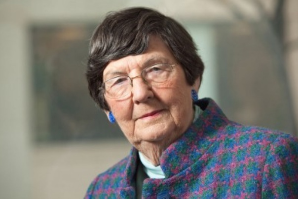 Portrait of a woman in a colorful coat with short, dark hair and glasses.